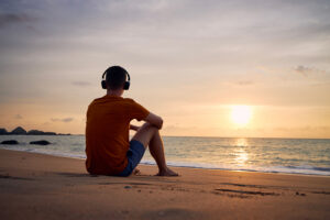 Man sitting on beach wearing headphones.